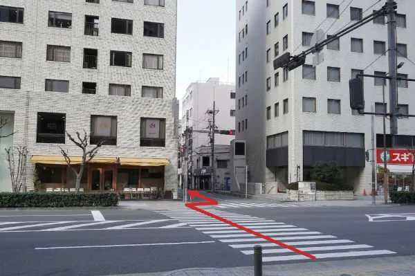 横断歩道のある交差点。左手にカフェ、右奥にスギ薬局。横断歩道を渡る方向への赤い矢印