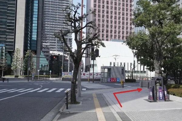 並木の続く広い道路と高層ビル群。右折を示す赤い矢印