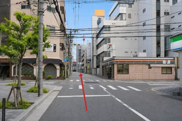 信号付きの交差点。右手にセブンイレブンとファミリーマート、前方を直進する方向の赤い矢印